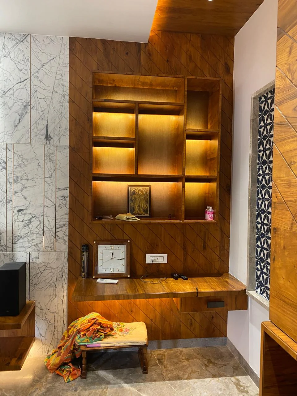 Backlit teak display shelving framed by a marble surround
