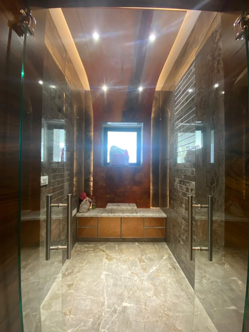Bathroom with a bronze-clad wall, frameless glass shower enclosure and a marble bench