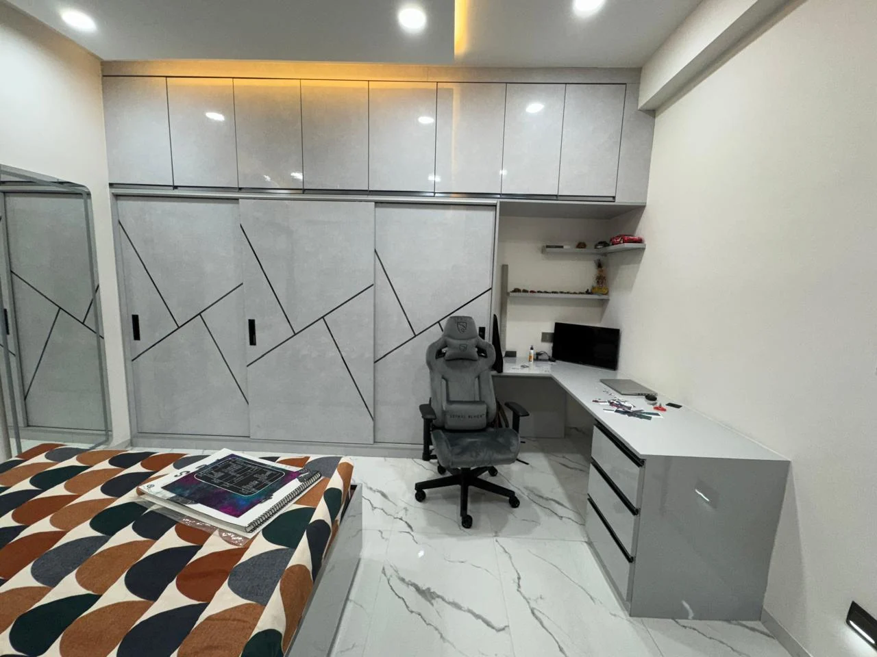 Bedroom with grey gloss wardrobes cut with geometric grooves and a study desk returning off the carcass