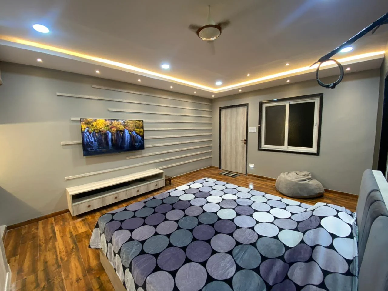 Completed bedroom with a horizontal slat panelled wall, wall-mounted television and warm timber flooring