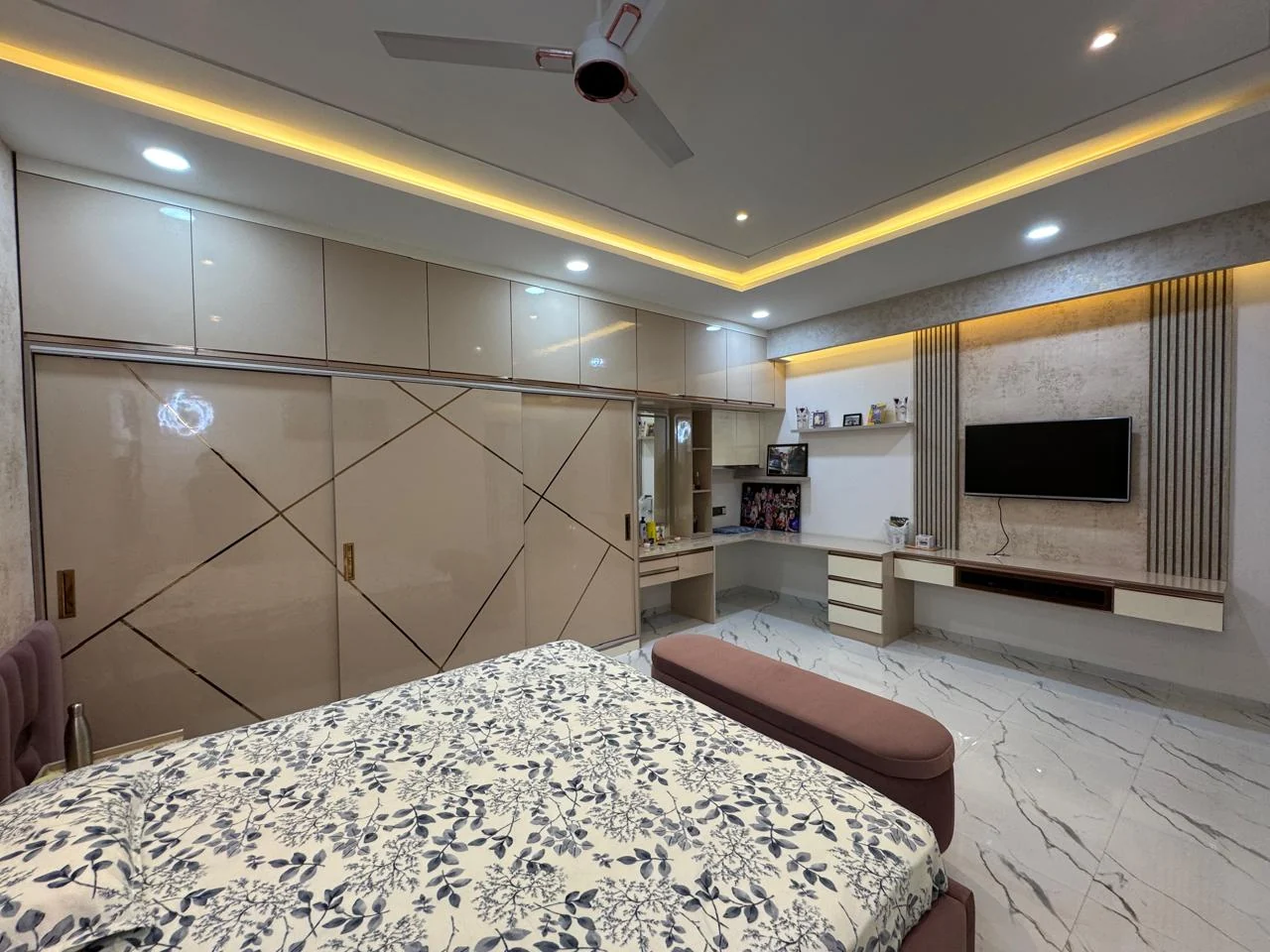 Bedroom with high-gloss wardrobes carrying rose-gold inlay lines and a television panel