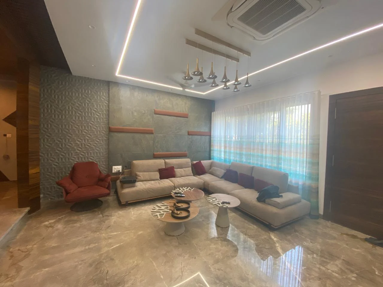 Living room with a cove-lit ceiling, a cluster of slim pendants and polished marble flooring