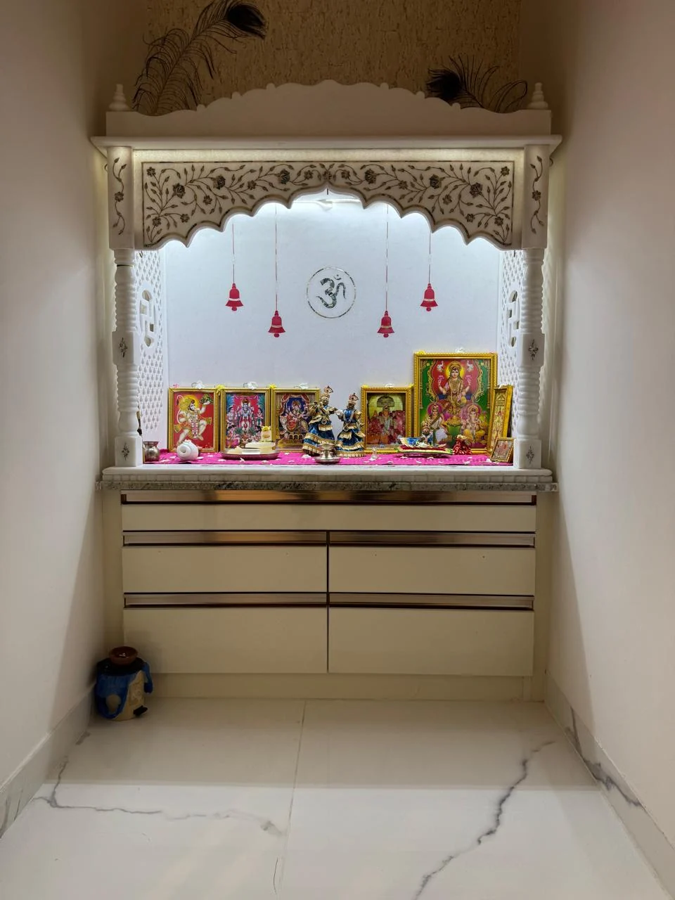 Pooja room with a carved white marble arch backlit above a run of storage drawers