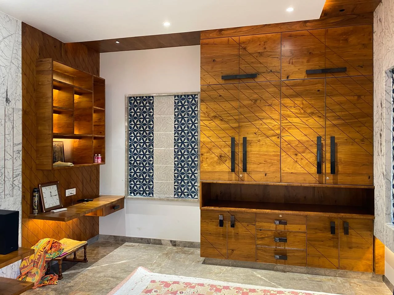 Solid teak wardrobe and study unit with diagonal grain, beside a patterned window panel and marble cladding
